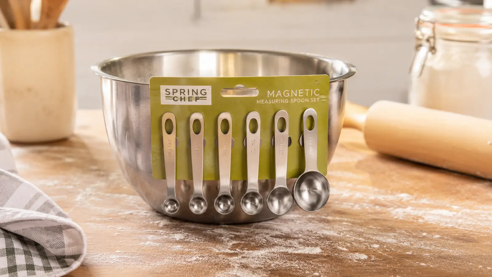 Magnetic measuring spoons held together on the side of a stainless steel mixing bowl