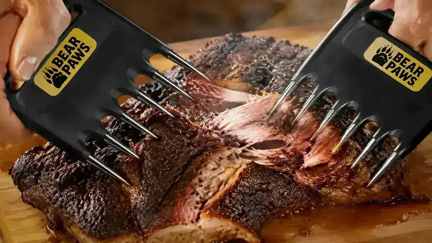 Close-up of meat claws with plastic tines pulling a bark-covered chunk of pork off the bone