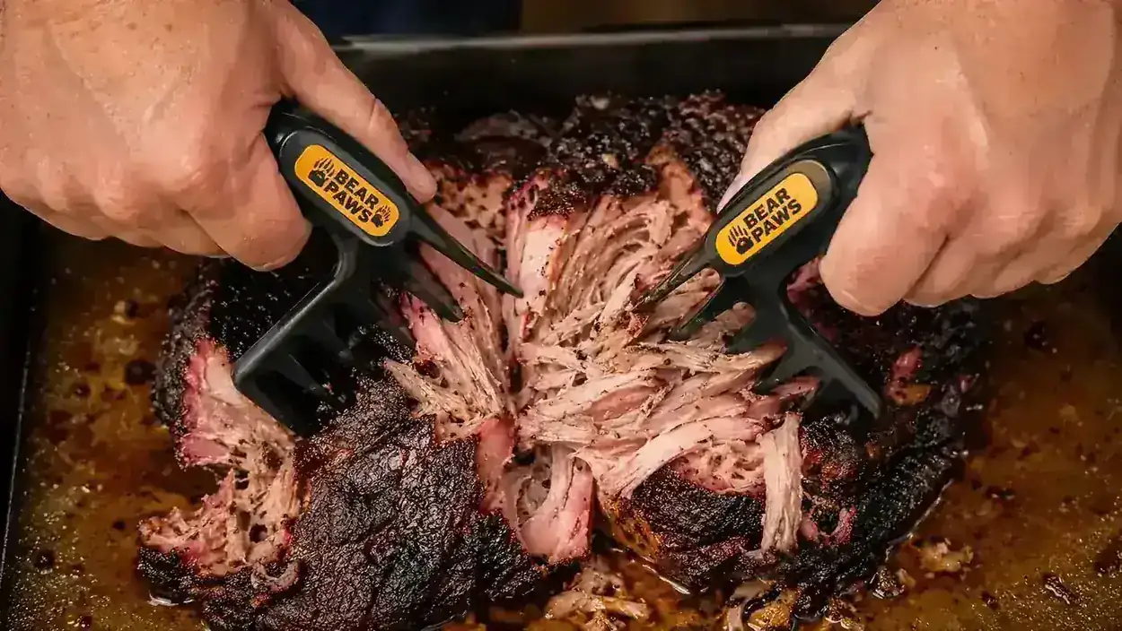 Close-up of meat claws digging into a pork shoulder and pulling a section of meat apart with the grain
