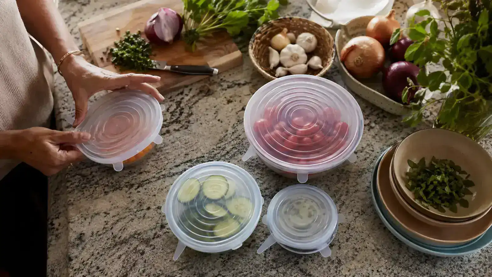 A set of colorful silicone stretch lids stretched over glass bowls of garden vegetables on a kitchen counter