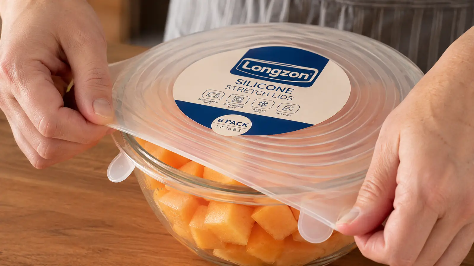 Hand stretching a silicone lid over a bowl of cut cantaloupe in a kitchen
