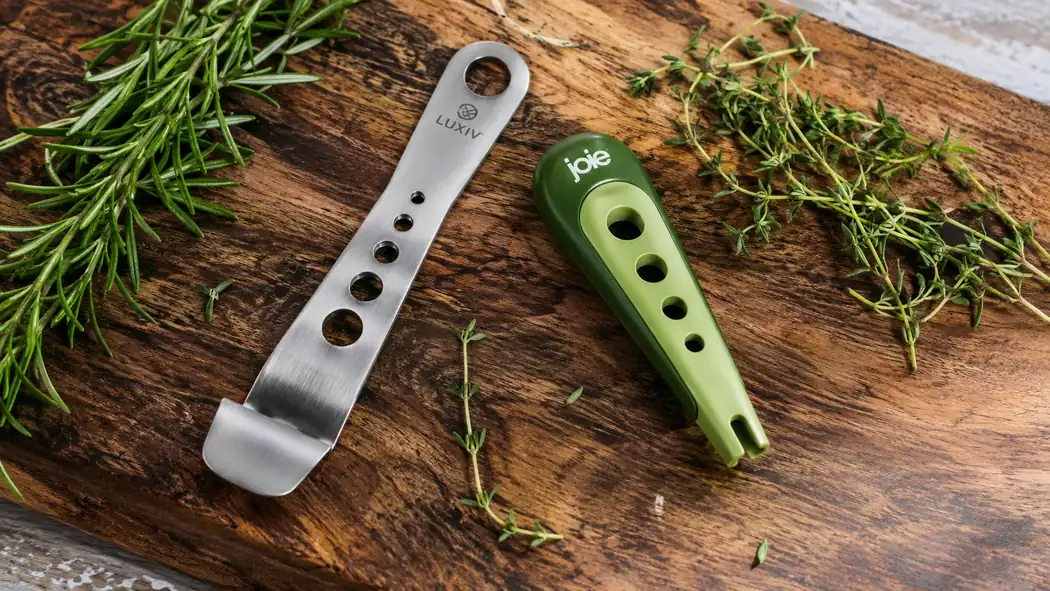 Two herb stripping tools laid side by side on a wooden cutting board next to fresh rosemary and thyme sprigs